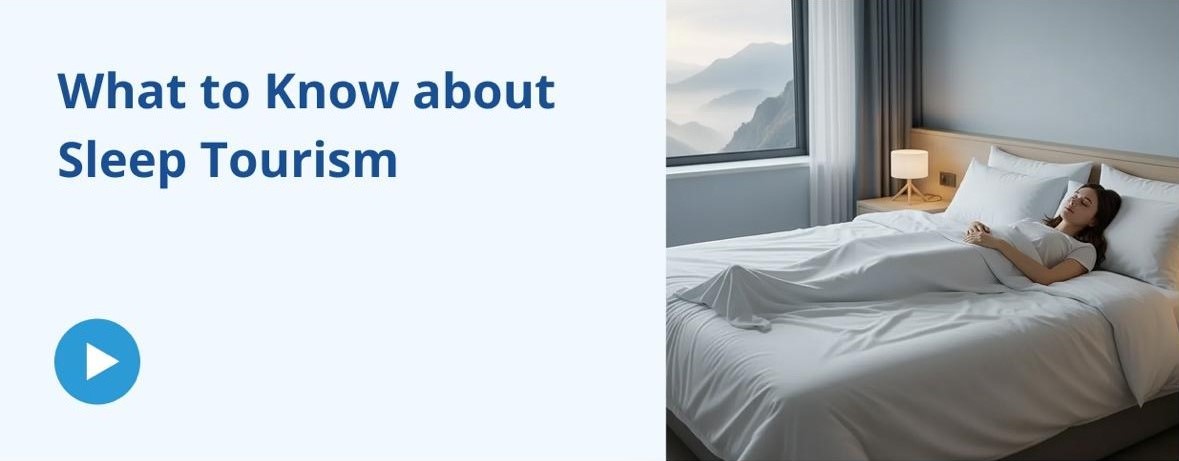 A split graphic or video thumbnail. The left side features a light blue background with dark blue text reading "What to Know about Sleep Tourism" above a blue circular play button icon. The right side shows a serene photo of a woman sleeping peacefully in a comfortable bed with crisp white linens. Next to the bed is a nightstand with a small, glowing lamp, and a large window reveals a calming view of a misty mountain landscape.