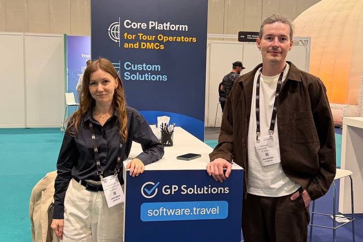 A man and a woman posing next to a blue GP Solutions information stand at the Travel Tech Show pavilion.