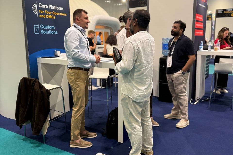 A GP Solutions representative in a white shirt and khaki pants talks with two attendees at a trade show.