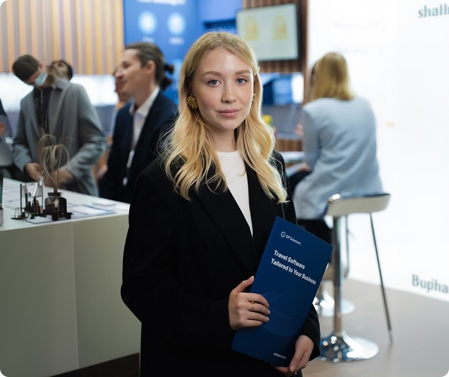Professional woman in a black blazer holding a blue brochure at a conference.
