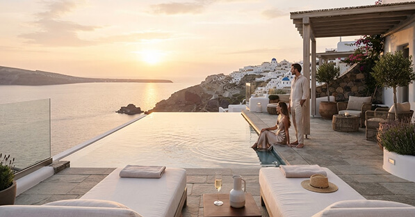 Sunset at a cliffside hotel infinity pool with lounge chairs, a man and a woman with a child by the pool edge.