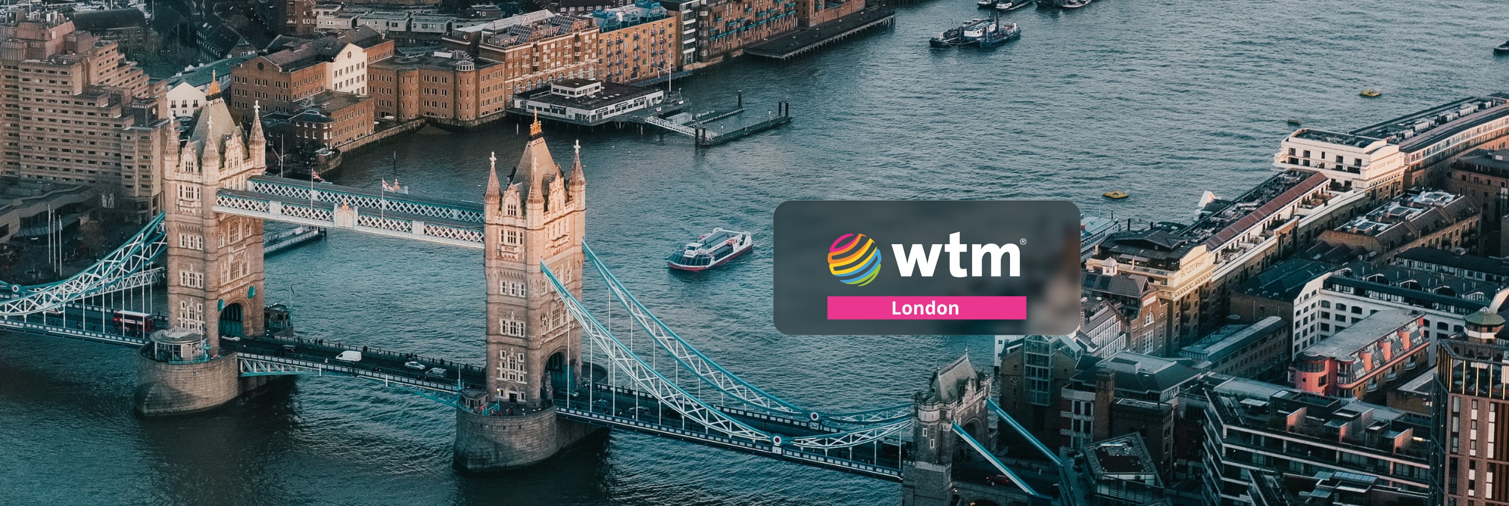 Aerial view of Tower Bridge in London with the Thames and surrounding buildings; overlayed with a dark rounded badge reading 'wtm London'.